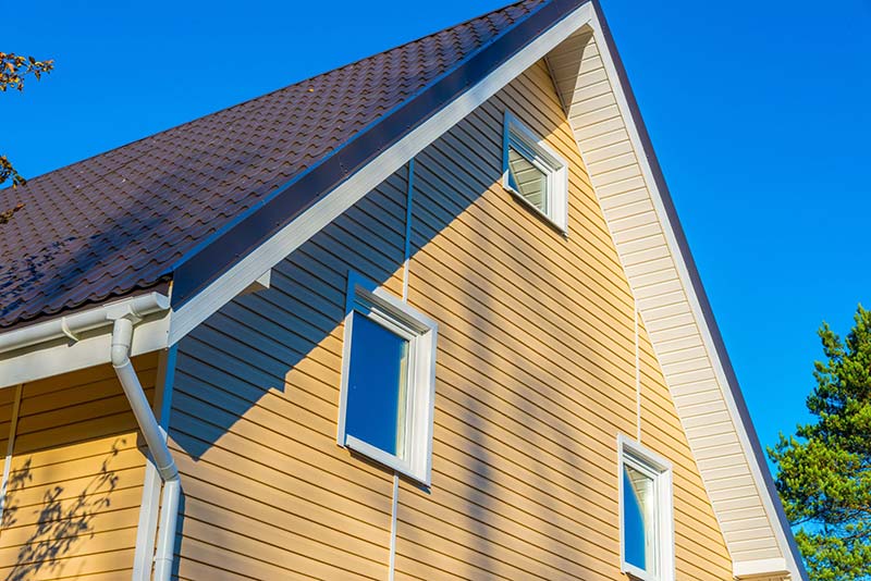 Wind damage siding and residential roofing repair on a beige Fargo, ND home with white-framed windows.