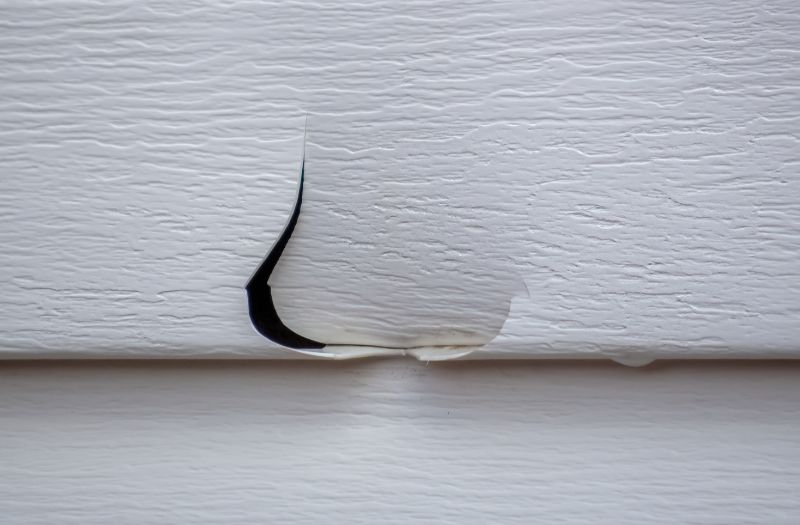 Close-up of a cracked and punctured vinyl siding panel requiring hail damage siding repair