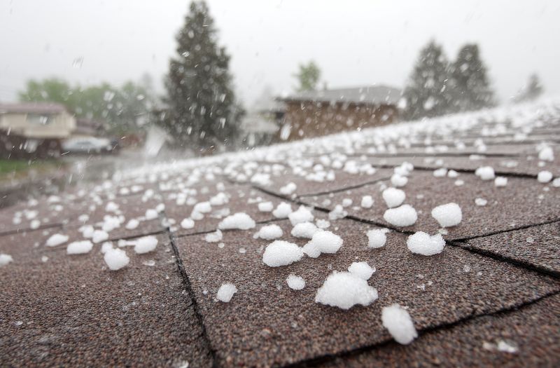 Heavy hail accumulating on asphalt roof shingles during a severe storm, illustrating storm damage insurance claims in Fargo.